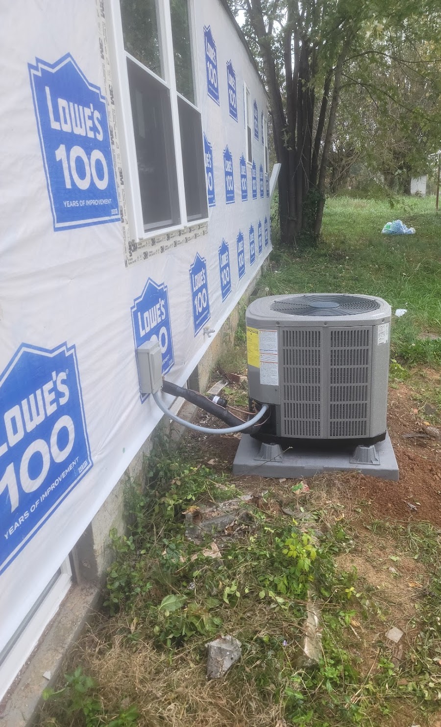 New residential AC condenser installed on a pad next to a home under construction